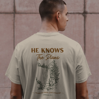 Man wearing a t-shirt with 'He Knows The Plans' text and design on the back.