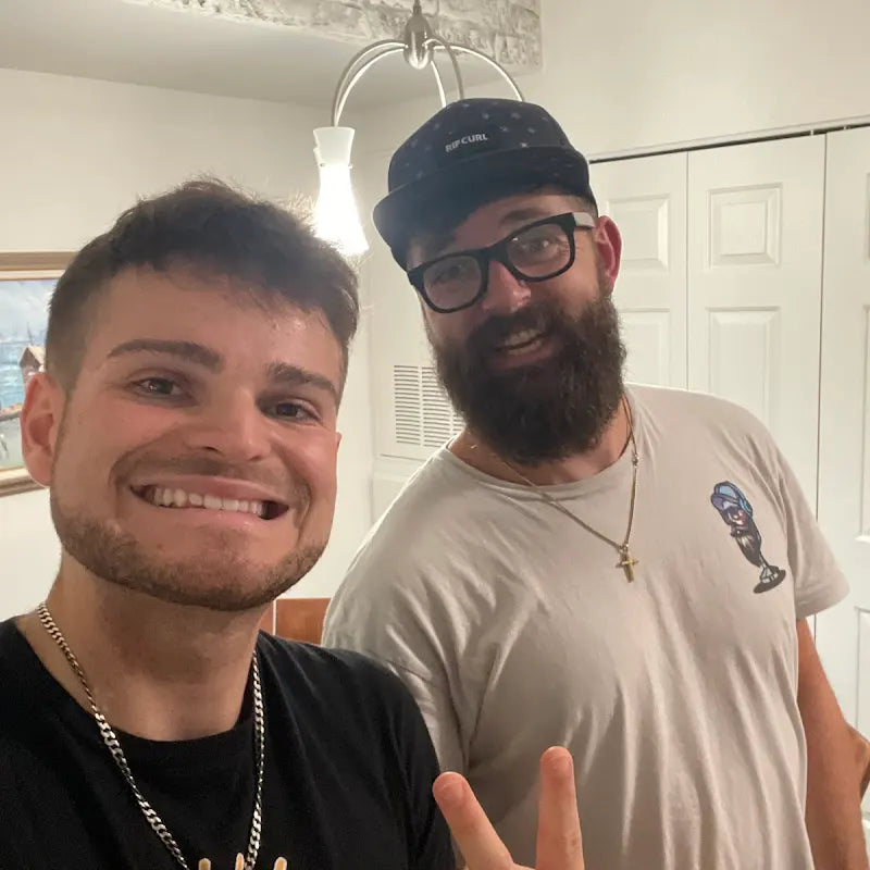 Two men posing for a photo in a room with white walls and a light fixture.